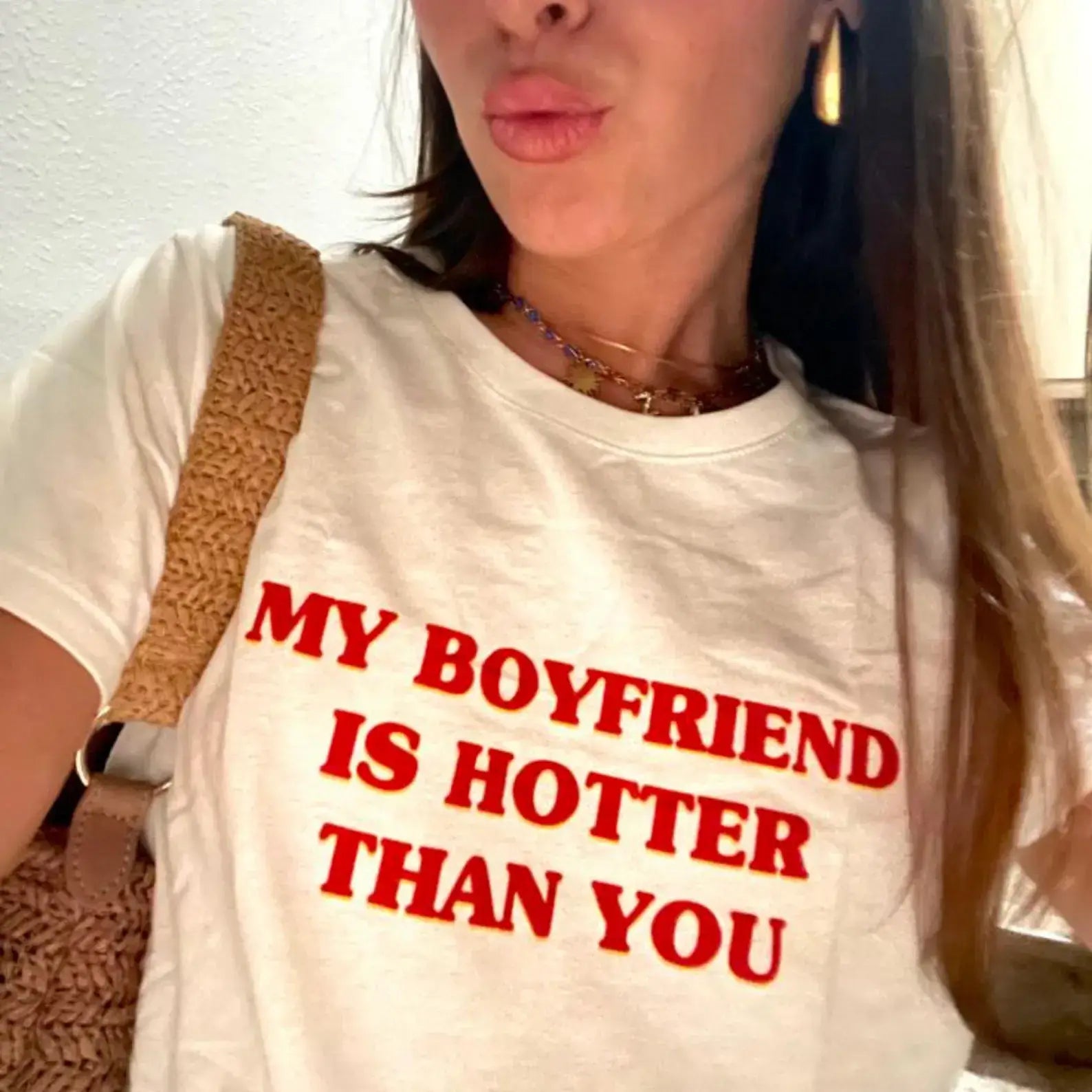 Woman wearing a white T-shirt with the phrase 'My Boyfriend Is Hotter Than You' in bold red letters.